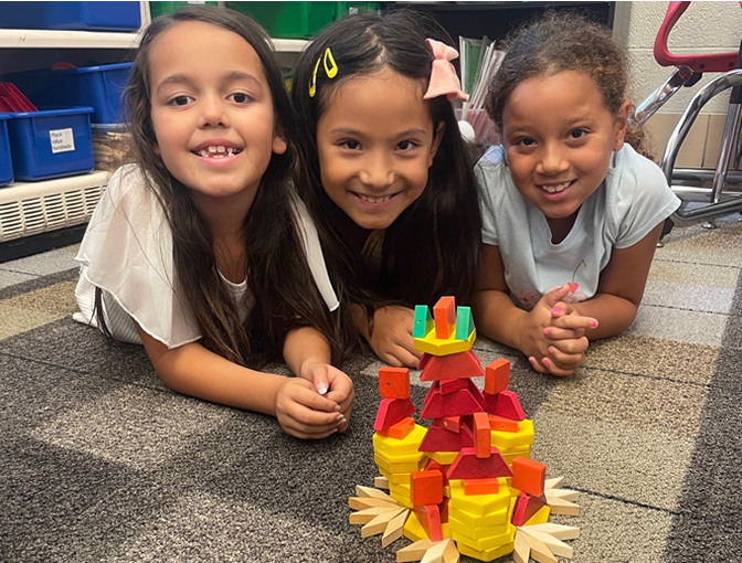 Three students pose with the structure they built with blocks.