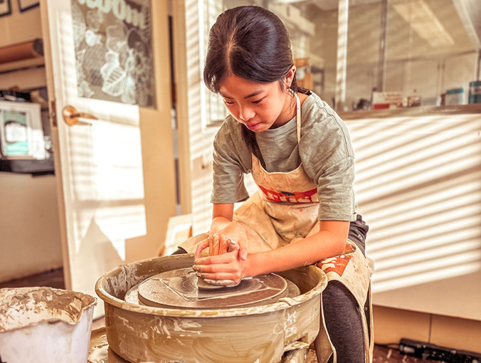 A student uses the pottery wheel to create a clay pot.