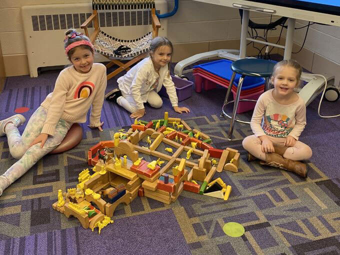 Three students pose with the structure they built with blocks.